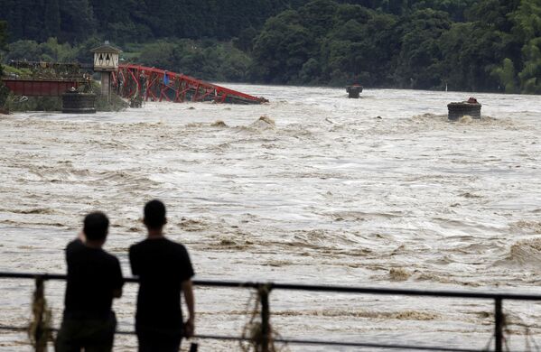 До сих пор 13 человек числятся пропавшими без вести. На фото - люди смотрят на вышедшую из берегов после сильных дождей реку Кумагава в городе Кумамура. Префектура Кумамото, юго-запад Японии - Sputnik Грузия