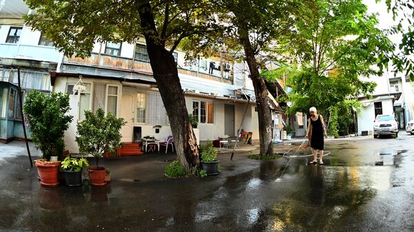 Женщина убирает двор утром в Тбилиси в жаркую погоду, поливая его водой - Sputnik Грузия