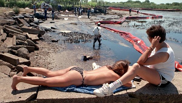 Отдыхающие рядом с рабочими во время очистки пляжа от нефти в Аргентине, 1999 год  - Sputnik Грузия