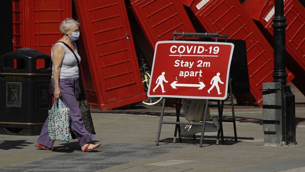 Женщина в медицинской маске и плакат с призывом соблюдать социальную дистанцию на фоне скульптуры британского скульптора Дэвида Маха Out of Order в Лондоне, Великобритания  - Sputnik Грузия