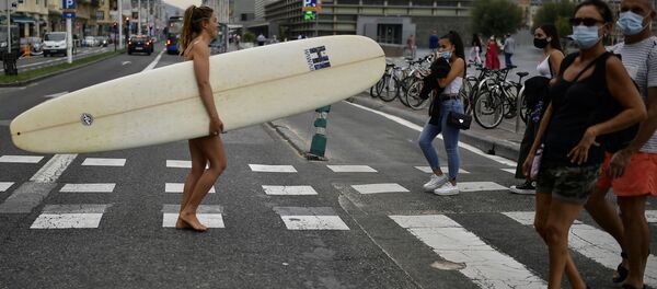 Девушка с доской для серфинга идет по улице Сан-Себастьян в Испании во время пандемии коронавируса COVID 19 - Sputnik Грузия