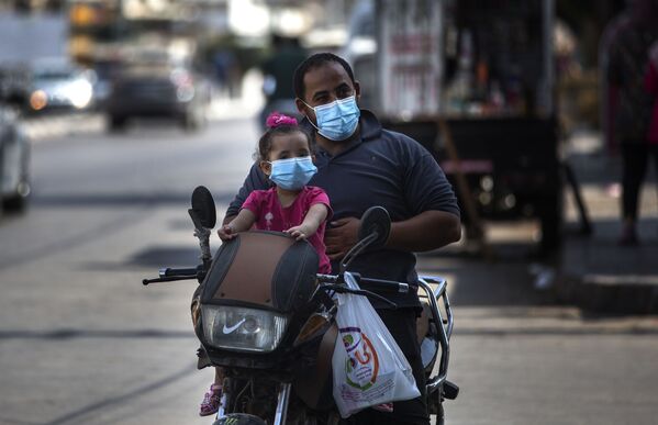 Палестинцы, отец с дочерью, едут в масках по делам на мотороллере в городе Газа. Они верят в опасность коронавируса - Sputnik Грузия