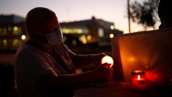 Женщина в масках зажигает свечи в память о погибших от коронавируса во время пандемии COVID 19 - Sputnik Грузия