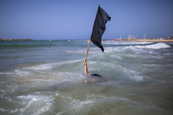 Мужчина, погрузившись в воду, держит в руке черный флаг. Так он выражает протест против закрытия пляжей из-за коронавируса. Тель-Авив, Израиль - Sputnik Грузия