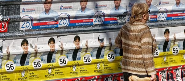 Предвыборная символика и пожилые люди. Женщина идет мимо предвыборных плакатов - Sputnik Грузия