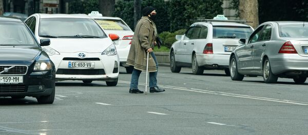 Пешеходы и коронавирус. Пожилая женщина в маске и с палкой переходит улицу в неположенном месте среди машин - Sputnik Грузия