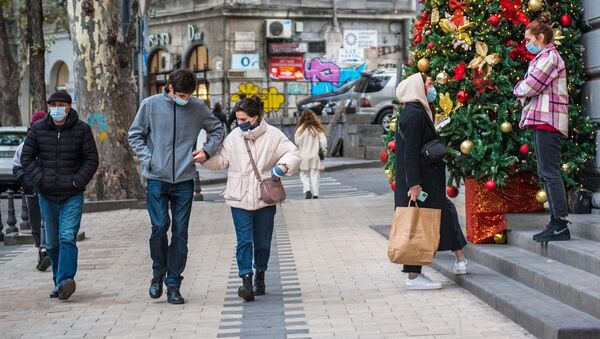 Эпидемия коронавируса - прохожие на улице в масках у новогодней елки - Sputnik Грузия