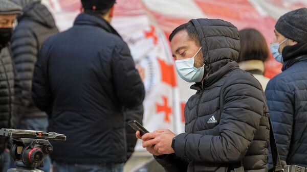 Эпидемия коронавируса - парень со смартфоном в капюшоне и в маске - Sputnik Грузия