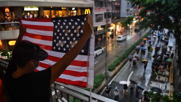 Мужчина держит флаг США над проходящими по улице Гонконга протестующими - Sputnik Грузия