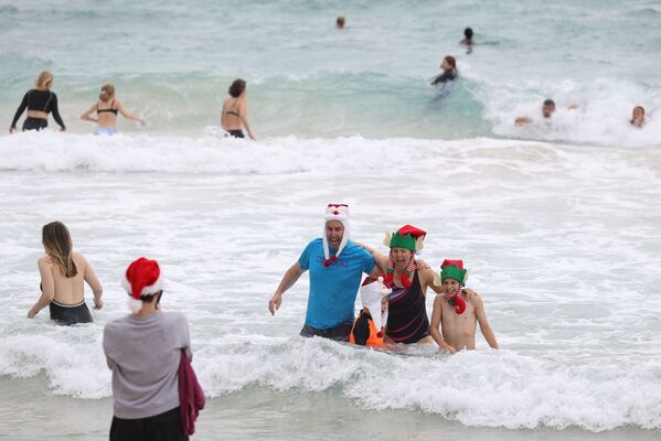 Люди в рождественской одежде позируют для фотографий в Рождество на пляже Бонди в Сиднее - Sputnik Грузия