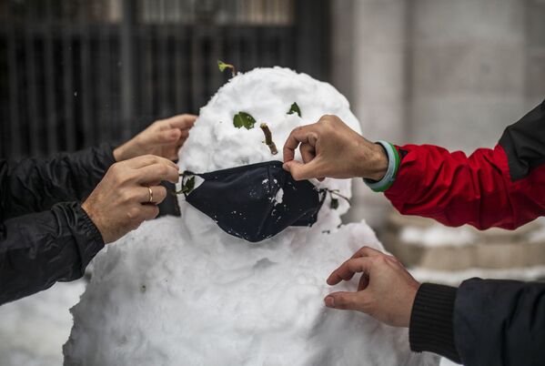 Не обошлось и без главного атрибута - защитной маски! Люди надевают маску на слепленного снеговика на одной из улиц в Мадриде - Sputnik Грузия