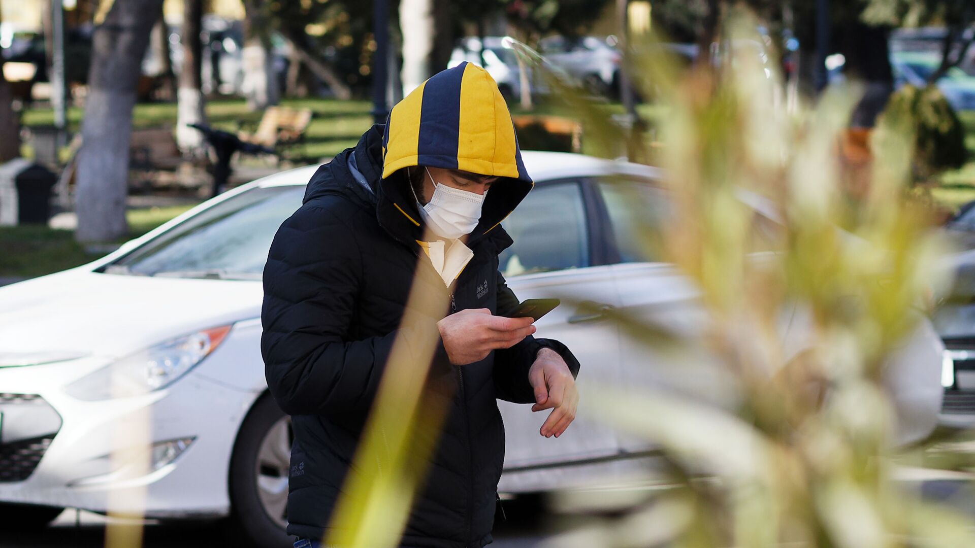 Эпидемия коронавируса - мужчина в маске и в капюшоне зимой со смартфоном идет по улице - Sputnik Грузия, 1920, 15.12.2021
