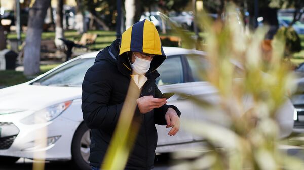 Эпидемия коронавируса - мужчина в маске и в капюшоне зимой со смартфоном идет по улице - Sputnik Грузия
