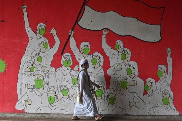 Мужчина-мусульманин проходит мимо фрески с изображением людей в масках во время пандемии коронавируса Covid-19 в Джакарте - Sputnik Грузия