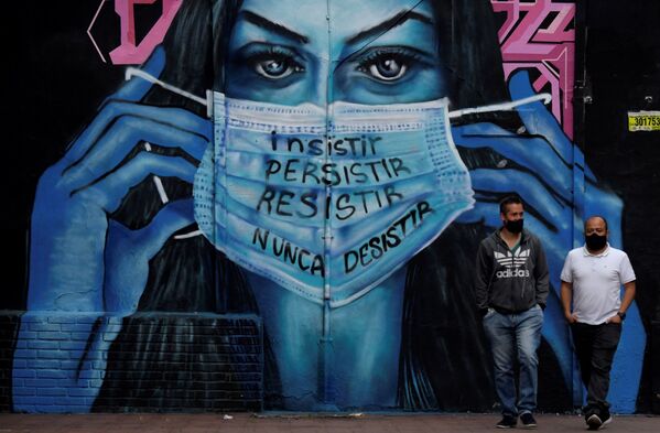 Мужчины в масках идут рядом с фреской с изображением женщины в маске с надписью Настаивайте, стойте, сопротивляйтесь, никогда не прекращайте в Колумбии - Sputnik Грузия