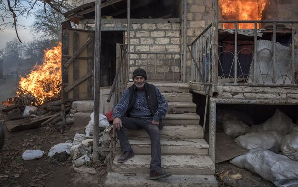 Местный житель Арег сидит у горящего дома в поселке Карегах, Нагорный Карабах - Sputnik Грузия