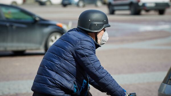 Эпидемия коронавируса - пожилой мужчина в каске и защитном респираторе едет на велосипеде по площади Свободы - Sputnik Грузия