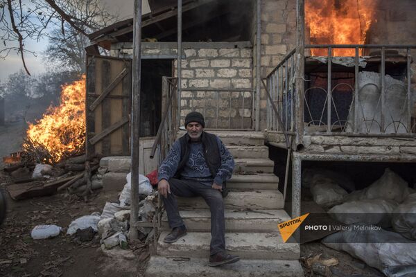 Местный житель Арег сидит у горящего дома в поселке Карегах. Некоторые жители сожгли свои дома перед тем как уйти - Sputnik Грузия