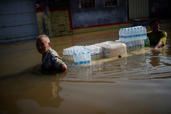 Жители деревни  в Синьсяне, провинция Хэнань, транспортируют по затопленным улицам питьевую воду. Наводнение вызвало не только проблемы с подачей воды, но и отключение электричества - Sputnik Грузия