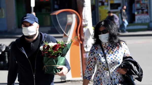Эпидемия коронавируса - прохожие на улице города в масках, мужчина несет цветы - Sputnik Грузия