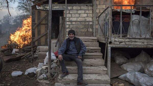 Местный житель Арег сидит у горящего дома в поселке Карегах, Нагорный Карабах. Некоторые жители сожгли свои дома перед тем как уйти - Sputnik Грузия