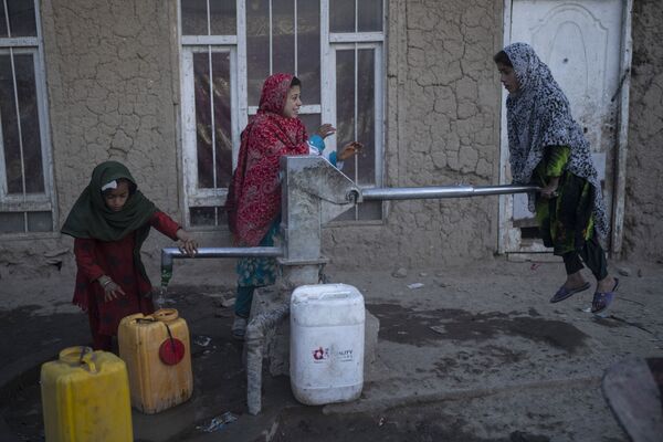 Девочки наполняют контейнеры водой с помощью ручного насоса в лагере для беженцев в Кабуле - Sputnik Грузия