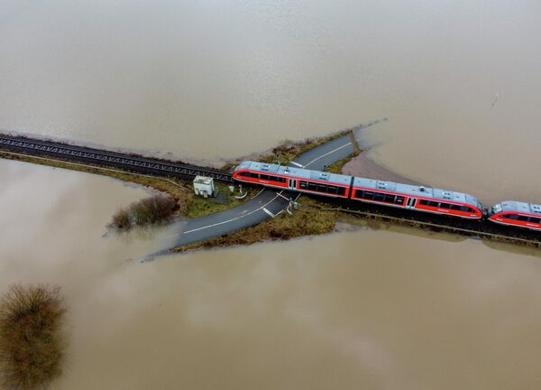 Поезд проезжает железнодорожный переезд, окруженный паводковыми водами из-за дождя и тающего снега в Ниддерау недалеко от Франкфурта, Германия. Февраль 2021 года. - Sputnik Грузия