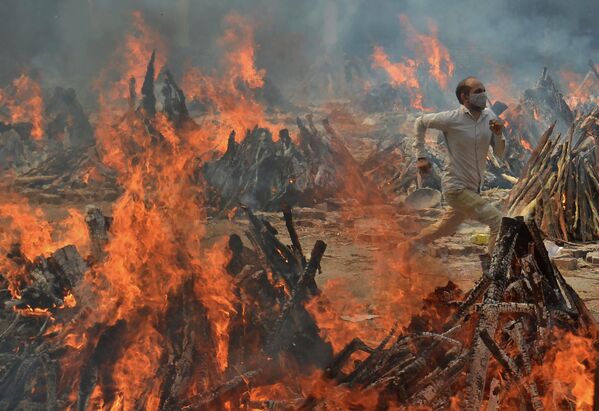 Мужчина бежит, спасаясь от жаркого огня десятков погребальных костров, сжигающих жертв COVID-19 в крематории на окраине Нью-Дели, Индия. - Sputnik Грузия
