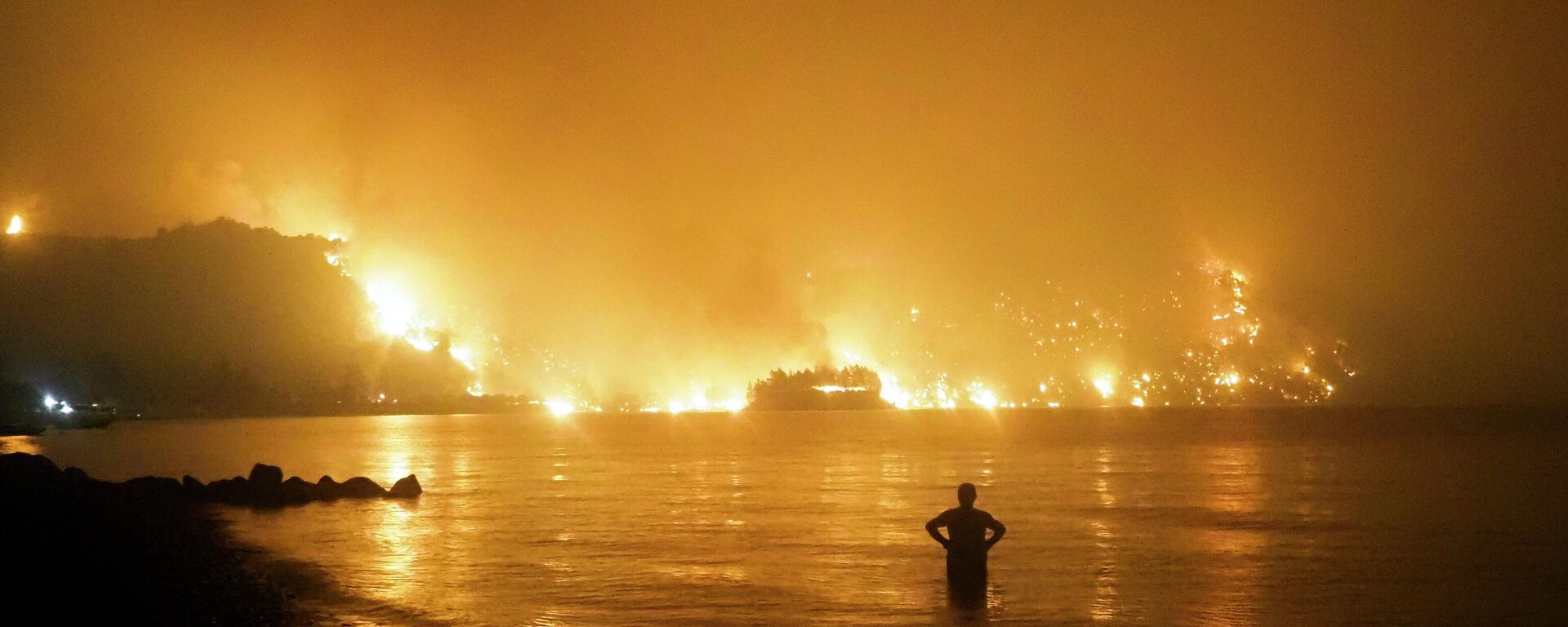 Мужчина наблюдает, как лесной пожар приближается к пляжу Кочили недалеко от деревни Лимни в Греции, примерно в 160 километрах к северу от Афин - Sputnik Грузия, 1920, 18.07.2022