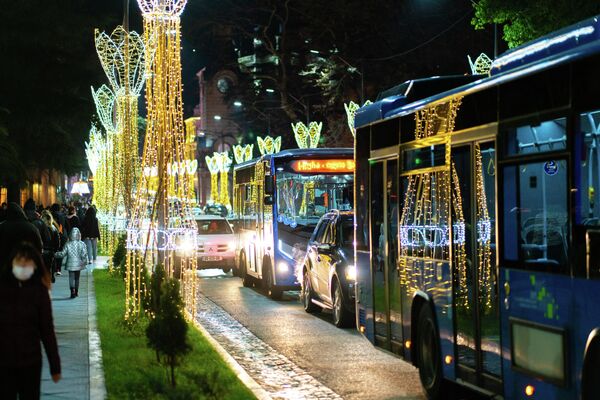 Огни новогодней иллюминации отражаются в стеклах автобусов, словно расширяя новогоднее пространство в другое измерение.  - Sputnik Грузия