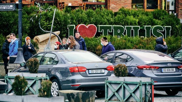 Эпидемия коронавируса и туризм - прохожие на улице в масках на фоне надписи Я люблю Тбилиси - Sputnik Грузия