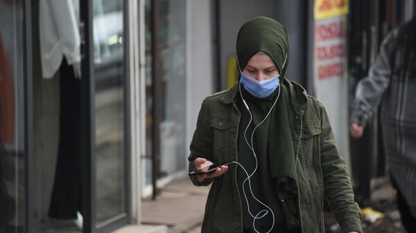 Эпидемия коронавируса - девушка в наушниках и со смартфоном идет по улице в маске - Sputnik Грузия
