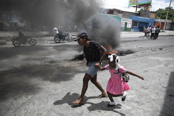 Женщина ведет ребенка мимо демонстрации против роста насилия в Порт-о-Пренс на Гаити - Sputnik Грузия
