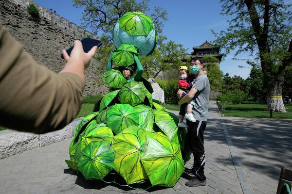 Мужчина с ребенком фотографируются рядом с работой под названием &quot;Защитите Землю с помощью зонтиков из банановых листьев&quot; китайской художницы Конг Нин  - Sputnik Грузия