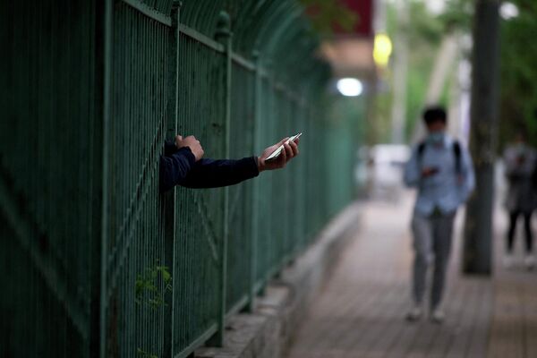 Житель с мобильным телефоном протягивает руку через забор в жилом районе, который находится под запретом, чтобы сдержать распространение Covid-19 в Пекине - Sputnik Грузия