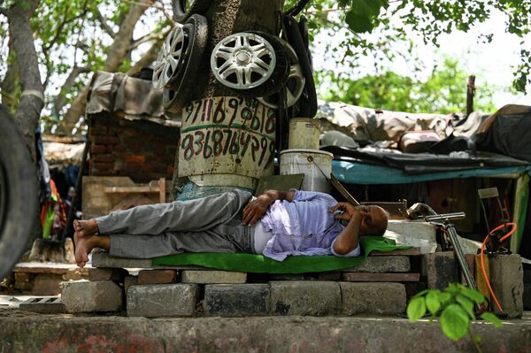 Как переждать такую жарищу? Мастер по шиномонтажу в ожидании клиентов в Нью-Дели спит в тени. - Sputnik Грузия
