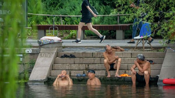 Женщина в маске проходит мимо мужчин, купающихся в жаркий день в Пекине - Sputnik Грузия