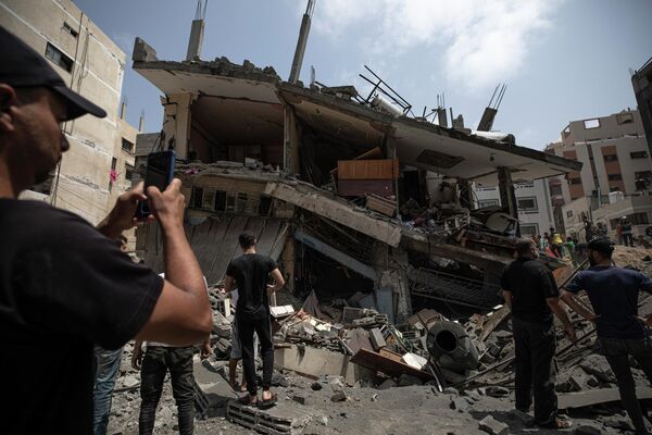 Палестинцы осматривают поврежденное жилое здание после того, как оно подверглось израильским авиаударам - Sputnik Грузия