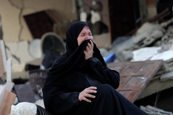 Реакция палестинской женщины, сидящей среди обломков своего дома, разрушенного во время ночных авиаударов Израиля по городу Газа - Sputnik Грузия