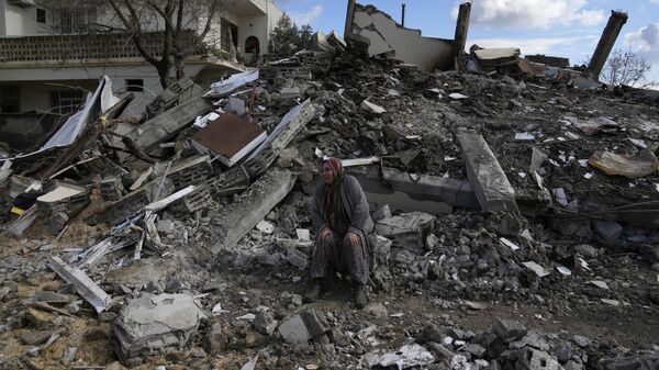 Женщина сидит на развалинах, пока спасатели ищут людей под остатками разрушенных зданий в городе Нурдаги, Турция - Sputnik Грузия