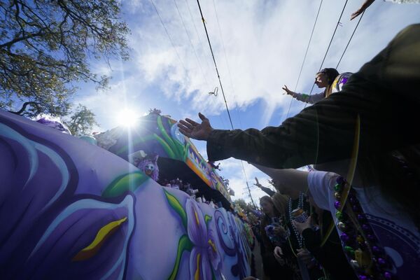 По улицам города движется карнавальная процессия с участием актеров и музыкантов в повозках. Участники шествия бросают в толпу различные памятные дары, в том числе игрушки, бусы и специальные медальоны с изображением символа парада - Sputnik Грузия