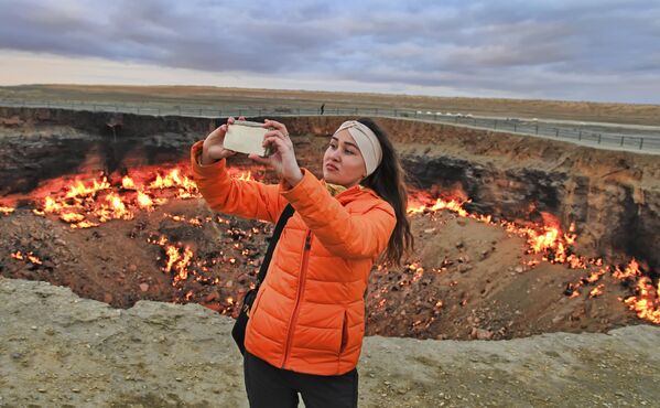 Девушка делает селфи на фоне горящего кратера &quot;Врата ада&quot; в пустыне Каракумы в Туркменистане. - Sputnik Грузия