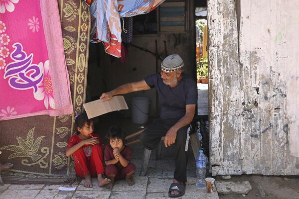 Пожилой житель Газы обдувает куском картона своих детей во время резкого повышения температуры. - Sputnik Грузия