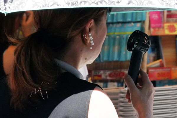 Девушка охлаждается с помощью переносного вентилятора на улице в Токио. - Sputnik Грузия