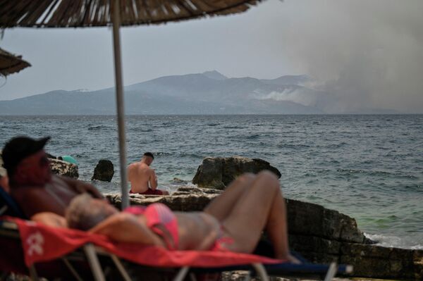 Люди загорают возле прибрежного города Саранда, когда клубы дыма поднимаются над греческим островом Корфу. - Sputnik Грузия
