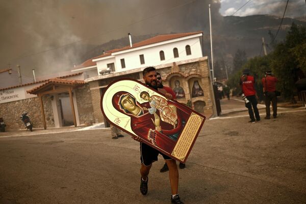 Доброволец выносит икону из горящего монастыря во время распространения лесного пожара в Афинах. - Sputnik Грузия