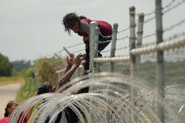 Мигранты, которые пересекли Рио-Гранде из Мексики в США, перелезают забор с колючей проволокой в Игл-Пасс, штат Техас. - Sputnik Грузия