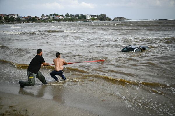 Люди пытаются вытащить автомобиль, затонувший в море в результате наводнения В Болгарии. - Sputnik Грузия