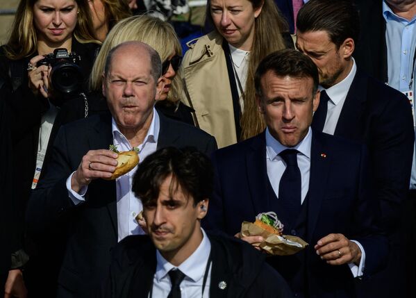 Канцлер Германии Олаф Шольц и президент Франции Эммануэль Макрон едят бутерброд с рыбой на пирсе в Гамбурге. - Sputnik Грузия