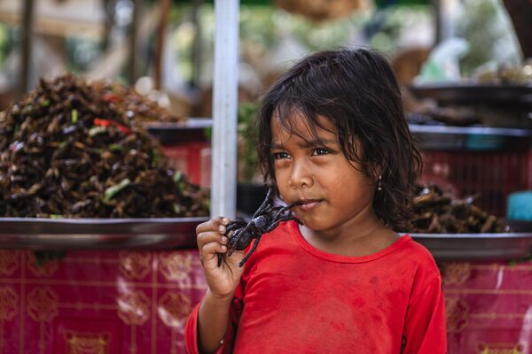 Девочка ест жареного паука на рынке в Камбодже. - Sputnik Грузия